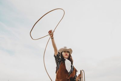 Low angle view of cowgirl throwing lasso while standing at ranch against sky