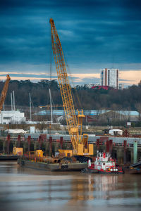 Crane at riverbank against cloudy sky