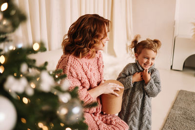 Side view of mother and daughter decorating christmas tree at home