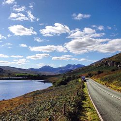 Lake and road by mountains against sky