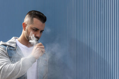 Young man smoking with an electronic cigarette over blue background