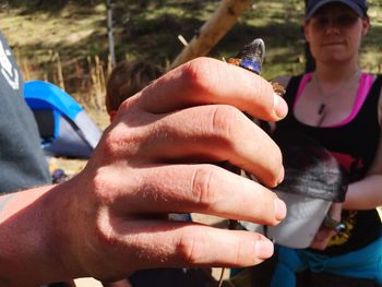 Cropped hand of person holding lizard with woman in background