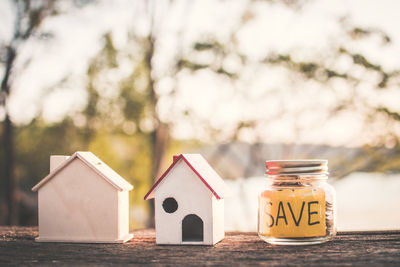 Close-up of model home with jar on wooden table against sky