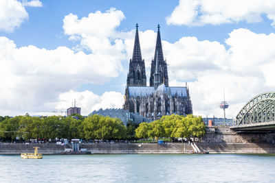 Scenic view of rhine river by cologne cathedral in city against sky