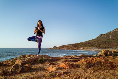 Woman standing on rock by sea against sky
