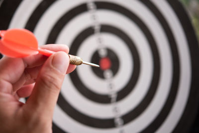 Close-up of hand holding dart against board