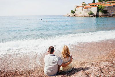 Rear view of couple sitting on beach against sea