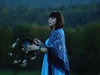 Woman holding dreamcatcher while standing in forest