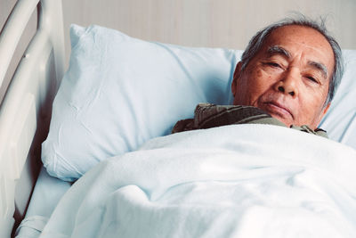 Portrait of senior man lying down on bed at hospital