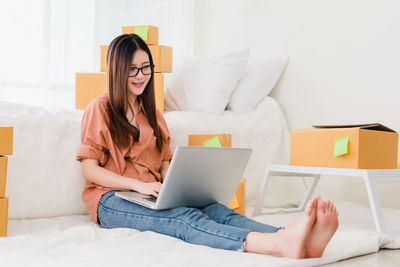 Midsection of woman using mobile phone while sitting on bed at home