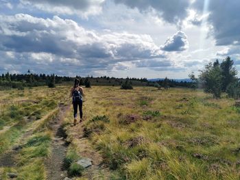 Rear view of woman walking on field against sky