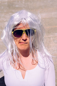 Portrait of woman wearing sunglasses and wig against wall