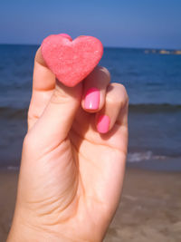 Midsection of hand holding heart shape over sea
