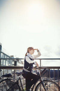 Young woman with bicycle on bridge against sky