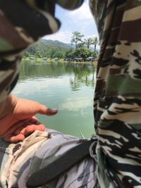 Close-up of hand feeding by lake against sky