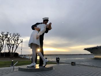 People standing by sculpture against sky during sunset