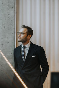 Thoughtful young businessman leaning on column in corporate office