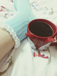 Low section of woman with coffee cup on bed