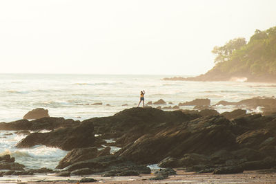 Distant view of woman standing on rock formations on shore at beach