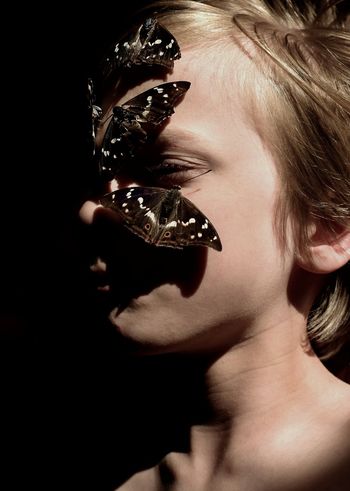 Close-up of boy with butterfly perching on face against black background