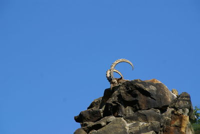 Low angle view of rocks against clear blue sky