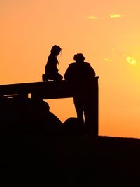 Low angle view of silhouette men standing against sky at sunset