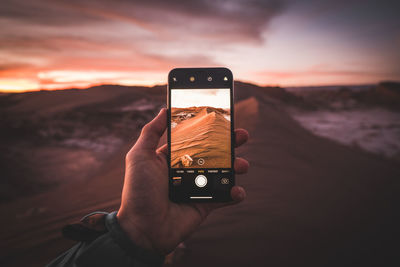 Cropped hand of tourist photographing sand dune with smart phone