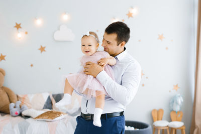Young happy dad holds a one-year-old smiling daughter in his arms in the children's room