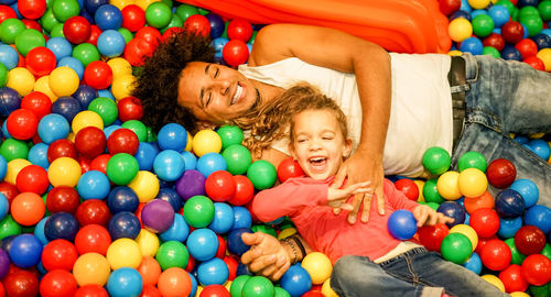 Happy father and daughter playing with multi colored balls in pool