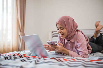 Young woman using mobile phone while sitting on bed at home