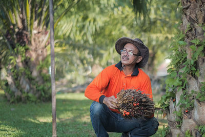 Smiling man holding fruits crouching by tree outdoors