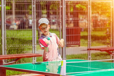 Boy playing table tennis during sunny day
