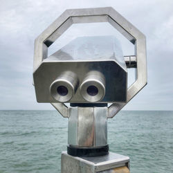 Close-up of coin-operated binoculars by sea against sky