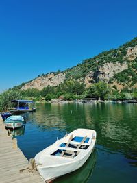 Boats moored on lake against clear blue sky