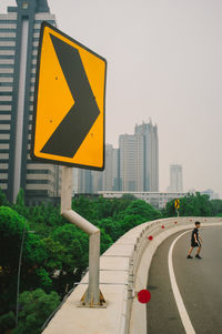 Road sign by street against sky in city