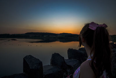 Side view of woman looking at sea against sky during sunset