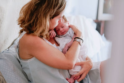 Closeup of loving mother holding adorable newborn baby while sitting on bed at home