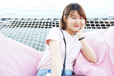 Portrait of smiling young woman sitting on net over lake