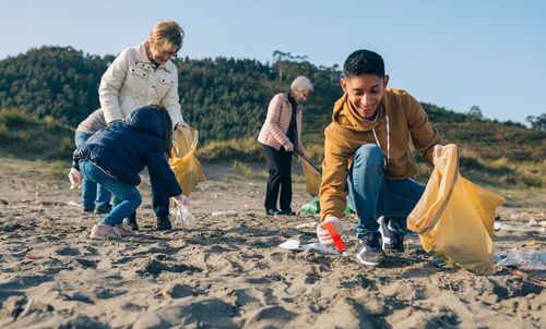 Young man picking up trash with group of volunteers on the beach
