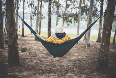 Rear view of woman sitting on swing in forest