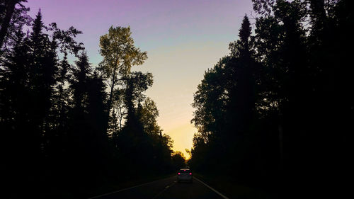 Road amidst silhouette trees against sky during sunset