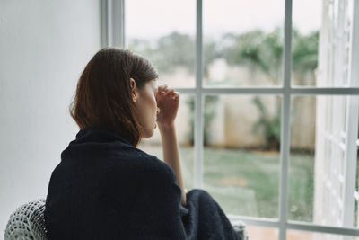 Side view of man looking through window at home