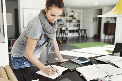 Female architect reading book at table in home office