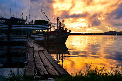 Boat moored on sea against dramatic sky during sunset