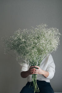 Woman holding white gypsophila blooming flowers, hiding behind bouquet