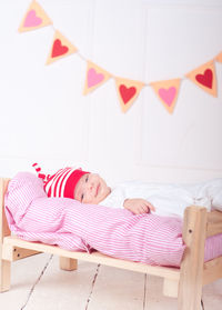 Cute baby wear pajamas and hat sleeping in small bed over white background with heart decoration