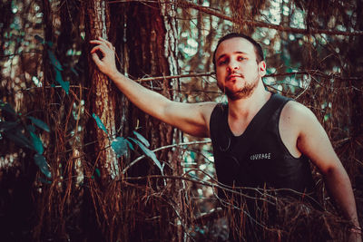 Young man standing by trees in forest