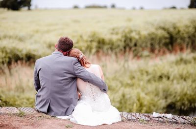 Rear view of newlywed couple sitting on retaining wall