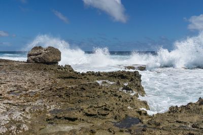 Waves splashing on rocks at shore against sky