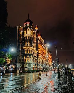 Illuminated building taj hotel by wet street against sky during rainy season